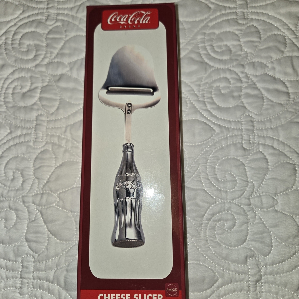 COCA-COLA 1997 NEW POLISHED CHROME W/CONTOUR BOTTLE HANDLE CHEESE SLICER 9 1/4"